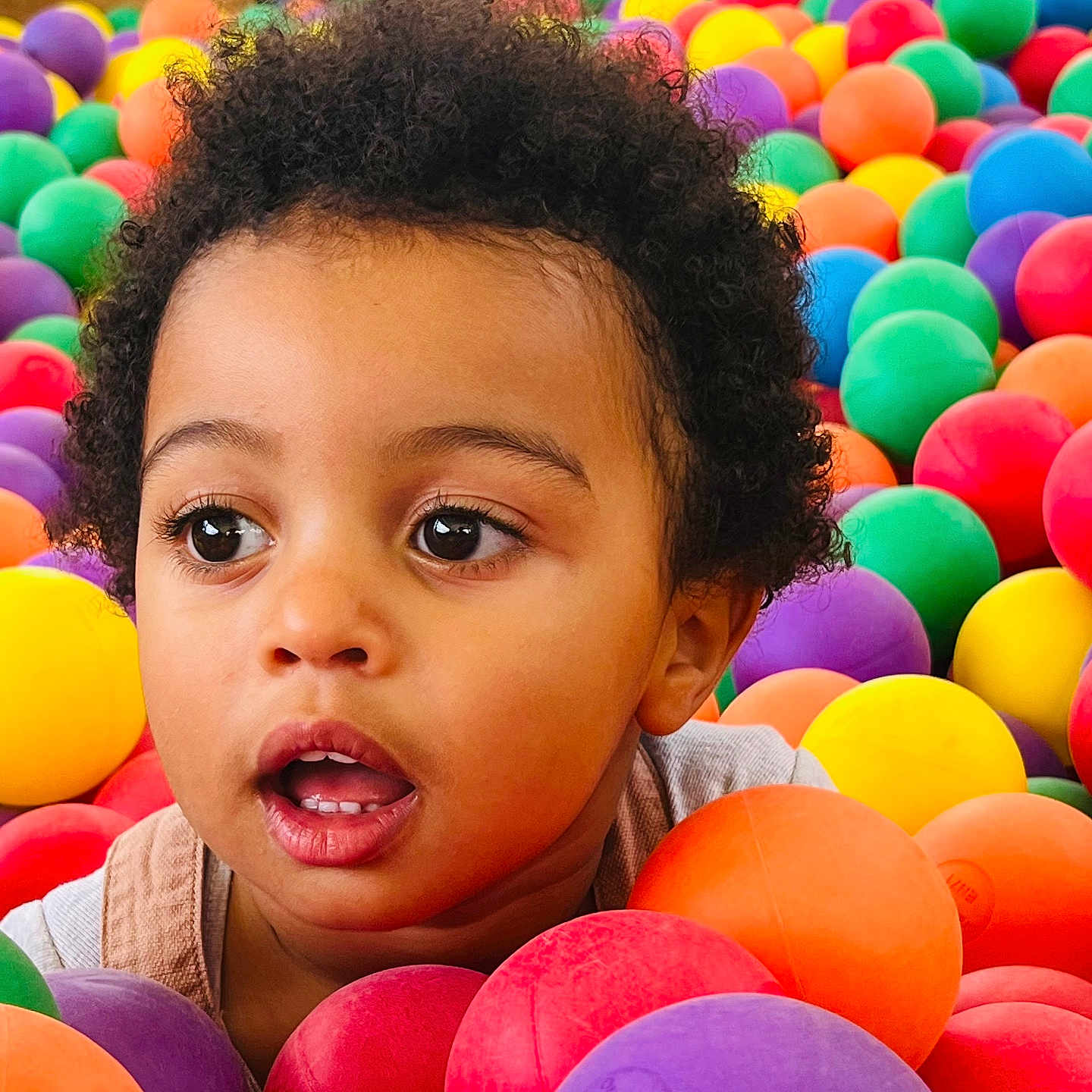 Ayden a rejoint le concours — aidez-le/la à gagner de superbes lots ! ball_pit, bright_colors, casual_clothing, child, closeup, colorful_balls, curly_hair, entertainment, expression, eye_contact, face, fun, happy, indoor, innocence, plastic_balls, play, portrait, toddler, young_child