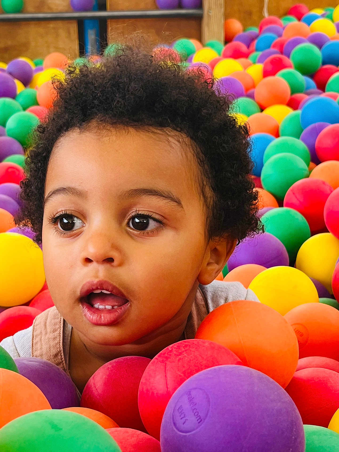 Ayden a rejoint le concours — aidez-le/la à gagner de superbes lots ! child, toddler, face, curly_hair, ball_pit, colorful_balls, play, expression, indoor, fun, young_child, portrait, bright_colors, plastic_balls, casual_clothing, closeup, happy, innocence, eye_contact, entertainment