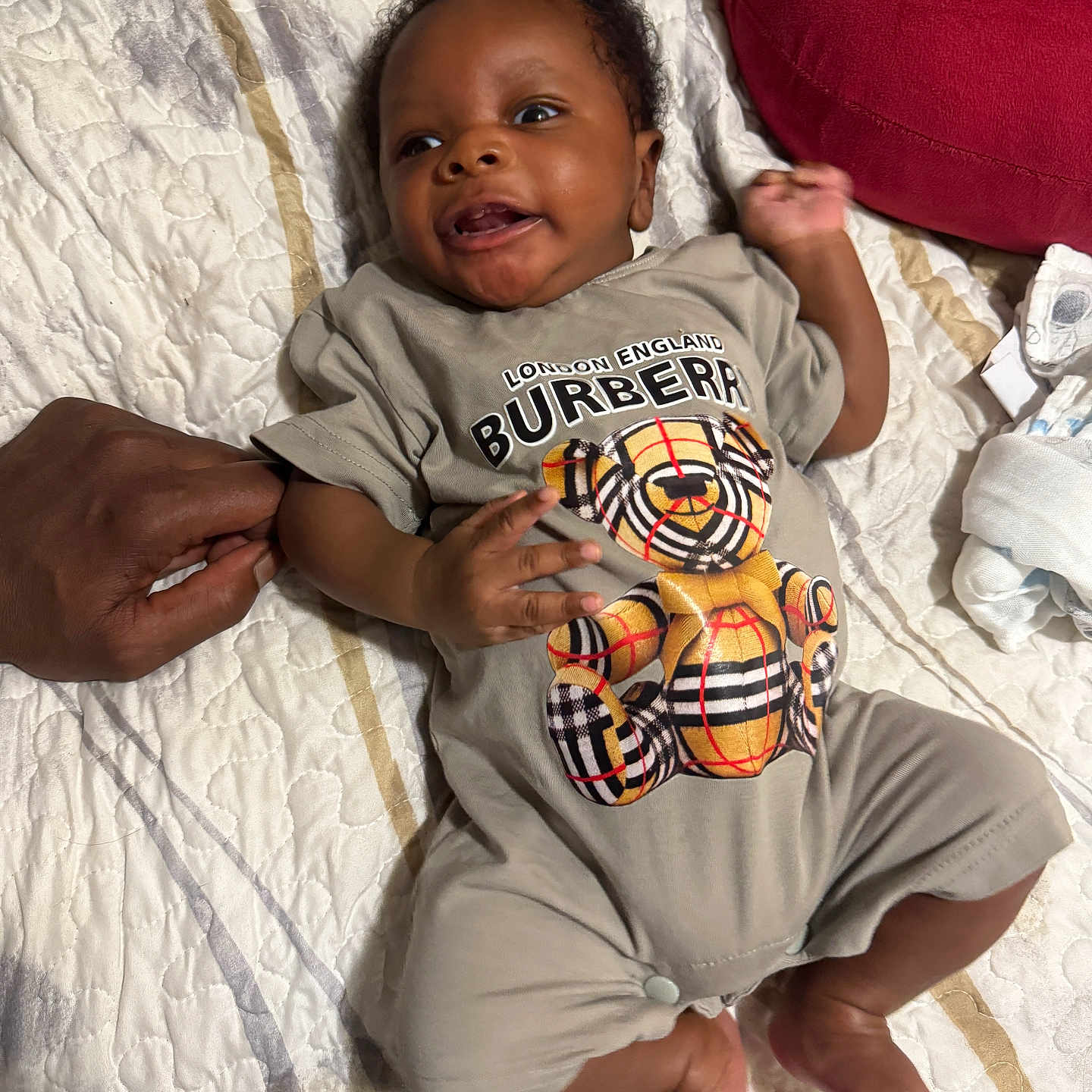 Tru joined the competition — help win amazing prizes! baby, infant, smiling, bedspread, quilt, clothing, bear, hand, adult_hand, lying_down, cute, child, person, fabric, foot, sleepwear, bedroom, red_pillow, comfort, soft