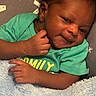 Tru is registered to the contest to win money with this photo: baby, infant, smiling, green_shirt, blanket, blue_blanket, hand, face, cheek, curly_hair, lying_down, cozy, soft_texture, fabric, pattern, cute, child, portrait, closeup, happy