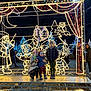 child, children, holiday_lights, night, balloon, winter_clothing, festive, outdoor, illumination, smile, beanie, jacket, platform, metal_structure, decorations, tree, owl, elf, people, crowd