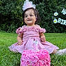 child, toddler, birthday, birthday_cake, pink_dress, party_hat, crown, smiling, happy, outdoor, garden, grass, cake, frosting, celebration, portrait, sitting, flowers, birthday_banner, family_event