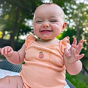 Layla is registered to the contest to win money with this photo: baby, child, infant, smiling, happy, onesie, peach, outdoor, nature, greenery, blurred_background, portrait, cute, skin, hand, sitting, expression, joy, face, person