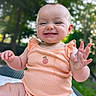 baby, child, infant, smiling, happy, onesie, peach, outdoor, nature, greenery, blurred_background, portrait, cute, skin, hand, sitting, expression, joy, face, person