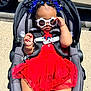 baby, car_seat, sunglasses, red_dress, headband, butterfly, outdoor, sunlight, child, fashion, accessory, cute, infant, seatbelt, summer, person, happy, legs, skin, fun