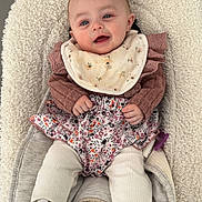 Inaya participe au concours pour gagner de l'argent avec cette photo : baby, infant, bib, sneakers, baby_seat, clothing, cute, smile, face, child, white_shoes, floral_pattern, warm_clothes, indoor, comfort, young_child, portrait, human, resting, cozy