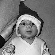 Romi participe au concours pour gagner de l'argent avec cette photo : baby, black_and_white, blanket, cute, eyes, face, festive, fingers, hand, headwear, holiday, indoor, infant, lying_down, mouth, nose, portrait, santa_hat, soft_texture, white_clothing