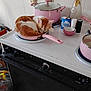 Ethan Lease is registered to the contest to win money with this photo: cat, orange_white_cat, frying_pan, pink_pot, stove, oven, countertop, salt_shaker, pepper_shaker, bowl, vase, flowers, lid, kitchen, cookware, curled_up, sleeping_cat, trash_bag, home_interior, stovetop