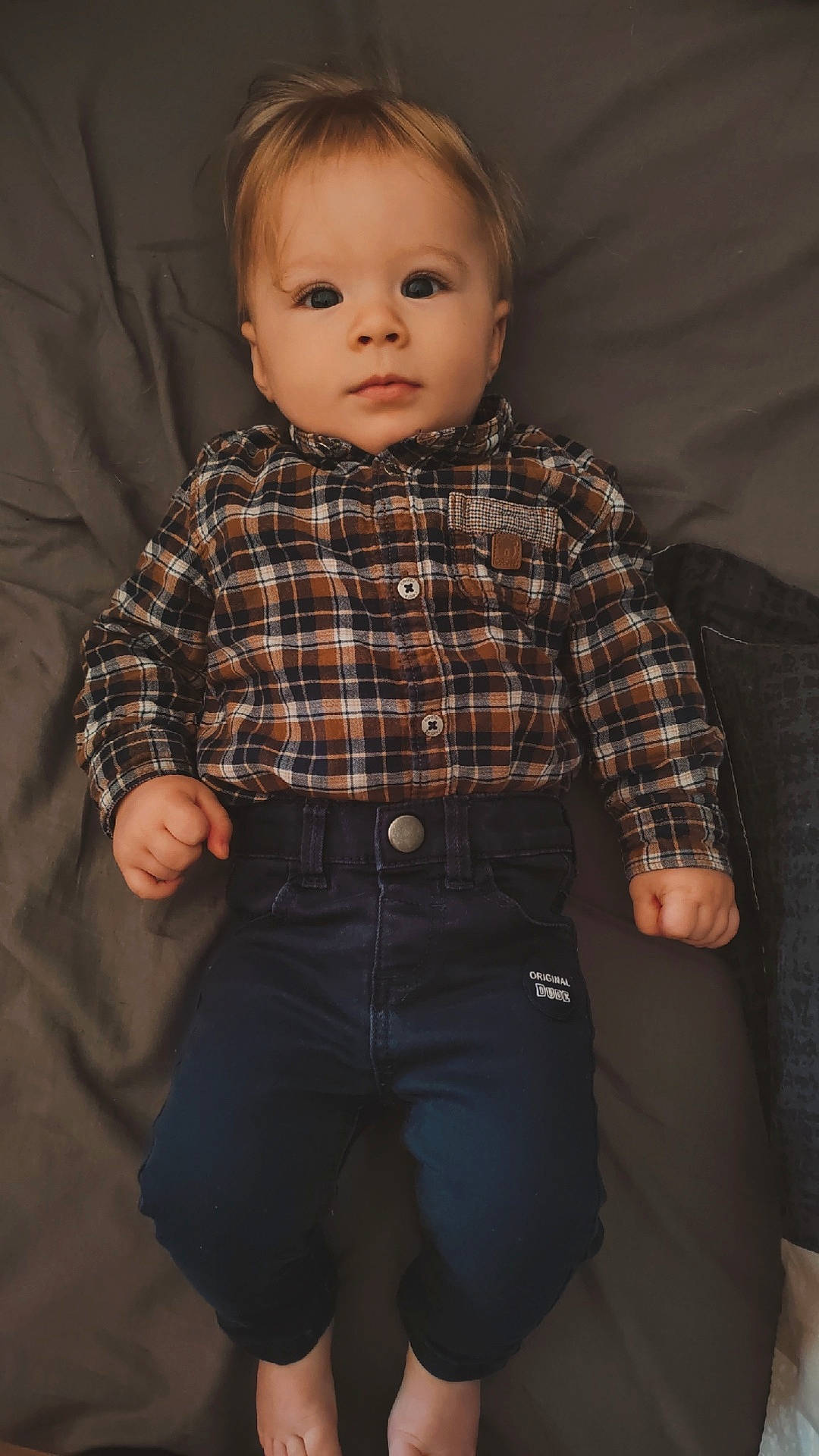 Evan participe au concours pour gagner de l'argent avec cette photo : baby, bed, calm, casual_clothing, child, curious, cute, dark_pants, face, feet, hands, head, indoors, infant, lying_down, person, plaid_shirt, portrait, skin, young