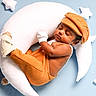 Hethav is registered to the contest to win money with this photo: baby, sleeping, orange_clothing, cap, mittens, crescent_moon_pillow, star_pillow, soft_toys, blue_background, infant, cozy, cute, resting, child, knitwear, newborn, portrait, comfortable, peaceful, indoor