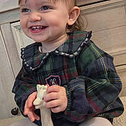 Haley a rejoint le concours — aidez-le/la à gagner de superbes lots ! child, toddler, smiling, toy, giraffe_toy, plaid_dress, hair_bow, indoor, holiday_decor, cabinet, white_tights, cute, happy, person, face, sitting, playful, furniture, warm_lighting, cheerful