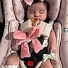 baby, infant, sleeping, car_seat, pink_bow, pacifier, plush_bow, floral_pattern, headband, white_clothing, safety_harness, child, cute, indoors, peaceful, soft_lighting, cushion, toddler, comfort, rest