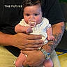 baby, pacifier, tattoo, watch, adult, holding, black_shirt, white_clothing, indoor, person, child, cute, portrait, hands, seated, expression, face, skin, hair, sitting