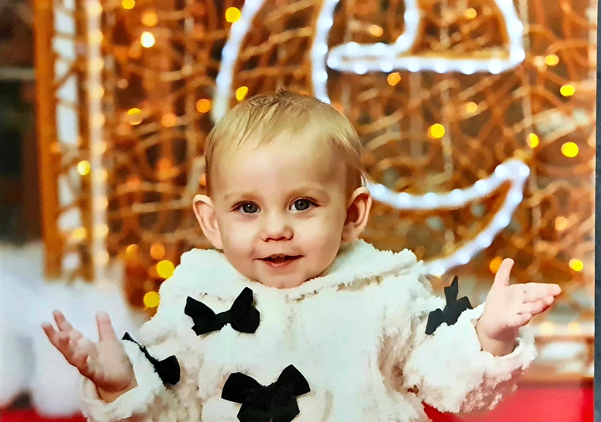 Aismée a rejoint le concours — aidez-le/la à gagner de superbes lots ! toddler, child, smiling, face, coat, white, black_bows, hands, indoors, portrait, cute, happy, baby, warm_lighting, decorative_lights, fashion, winter_clothing, expression, young_child, festive