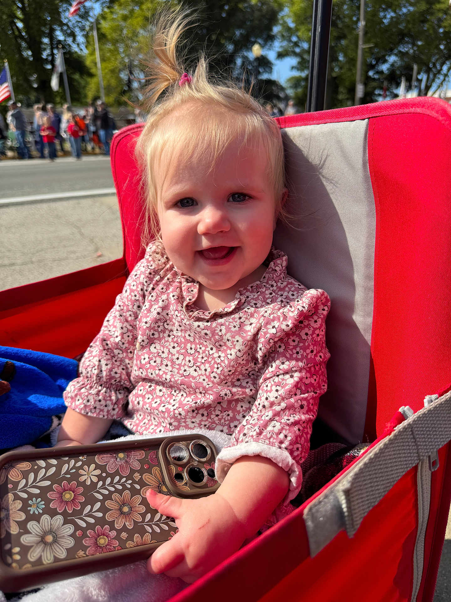 Cheyenne joined the competition — help win amazing prizes! toddler, child, smiling, stroller, red, phone, floral_pattern, outdoor, daylight, face, hair, clothing, hand, park, flag, people, tree, happy, person, cute