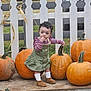 Delilah joined the competition — help win amazing prizes! toddler, child, pumpkin, autumn, outdoor, fence, grass, clothing, boots, curly_hair, striped_shirt, green_dress, fall, nature, small_person, standing, exploring, garden, seasonal, daylight