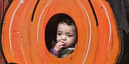 Delilah joined the competition — help win amazing prizes! child, toddler, pumpkin, cutout, face, orange, green_leaves, curious, thoughtful, portrait, costume, autumn, holiday, decoration, outdoor, cute, young_child, baby, person, festive