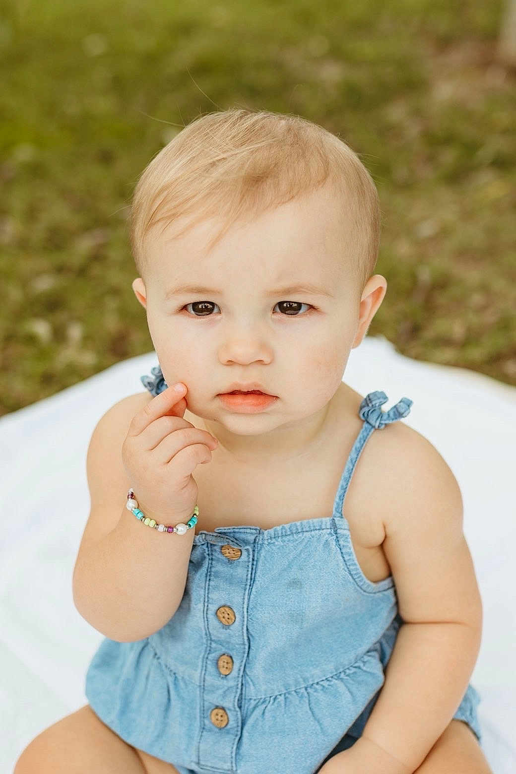 Miley joined the competition — help win amazing prizes! toddler, child, denim_dress, bracelet, outdoor, blanket, grass, cute, portrait, baby, person, skin, face, expression, sitting, young_child, summer, casual_clothing, natural_light, curious