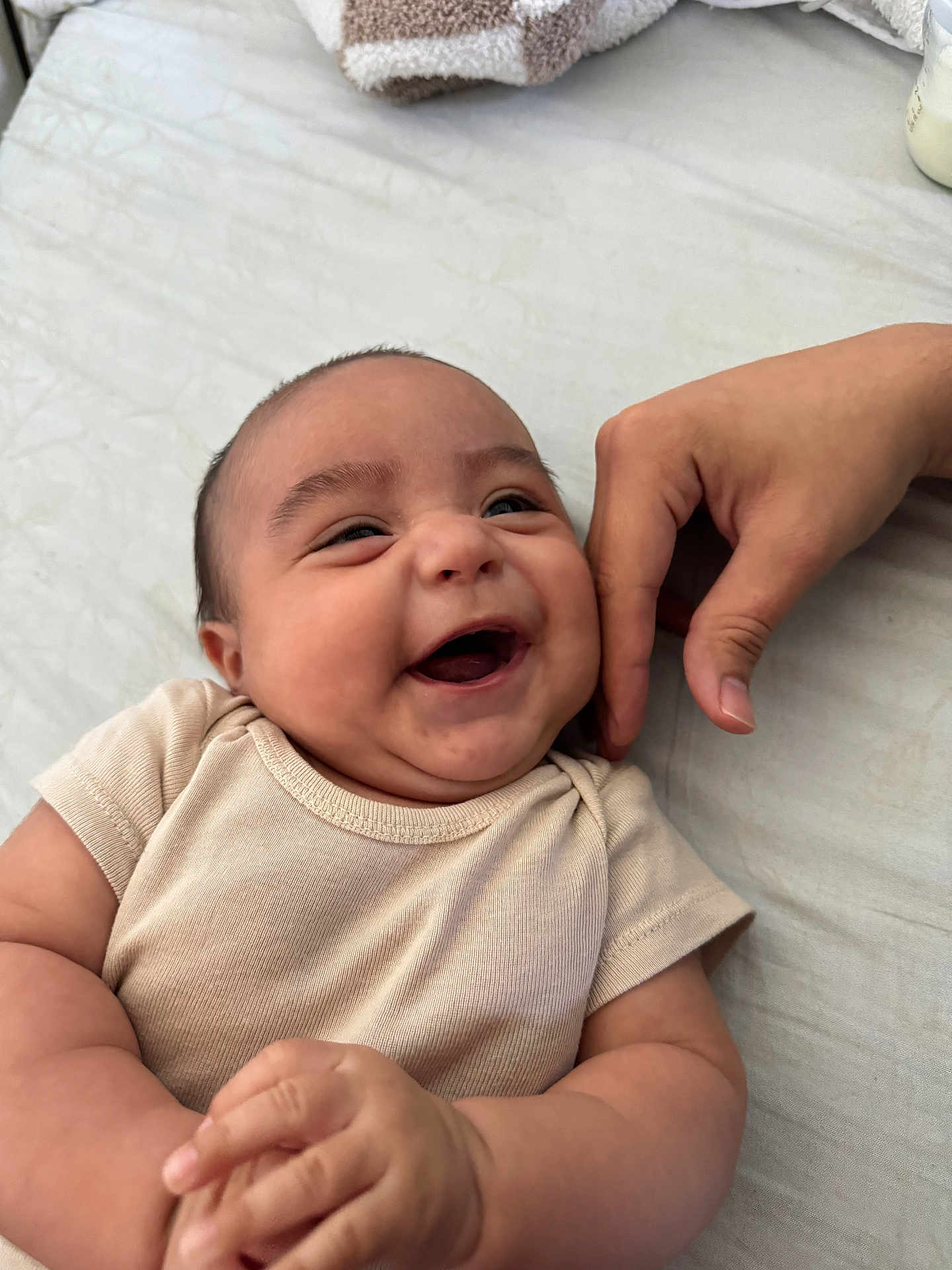 Amir is registered to the contest to win money with this photo: baby, infant, smiling, laughing, hand, onesie, cheek, skin, person, happy, cute, closeup, towel, bed, fabric, sleepwear, joy, expression, indoor, child