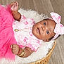 baby, basket, bow, bracelet, child, curly_hair, cute, floor, fluffy_blanket, headband, indoor, infant, jewelry, lying_down, necklace, pink_clothing, portrait, smiling, tutu, wooden_floor