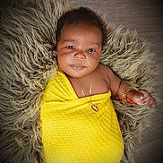 Ciana joined the competition — help win amazing prizes! adorable, baby, bracelet, child, cozy, cute, face, fluffy_rug, gold_jewelry, hand, indoor, infant, lying_down, necklace, portrait, skin, smiling, soft_texture, wrapped, yellow_blanket