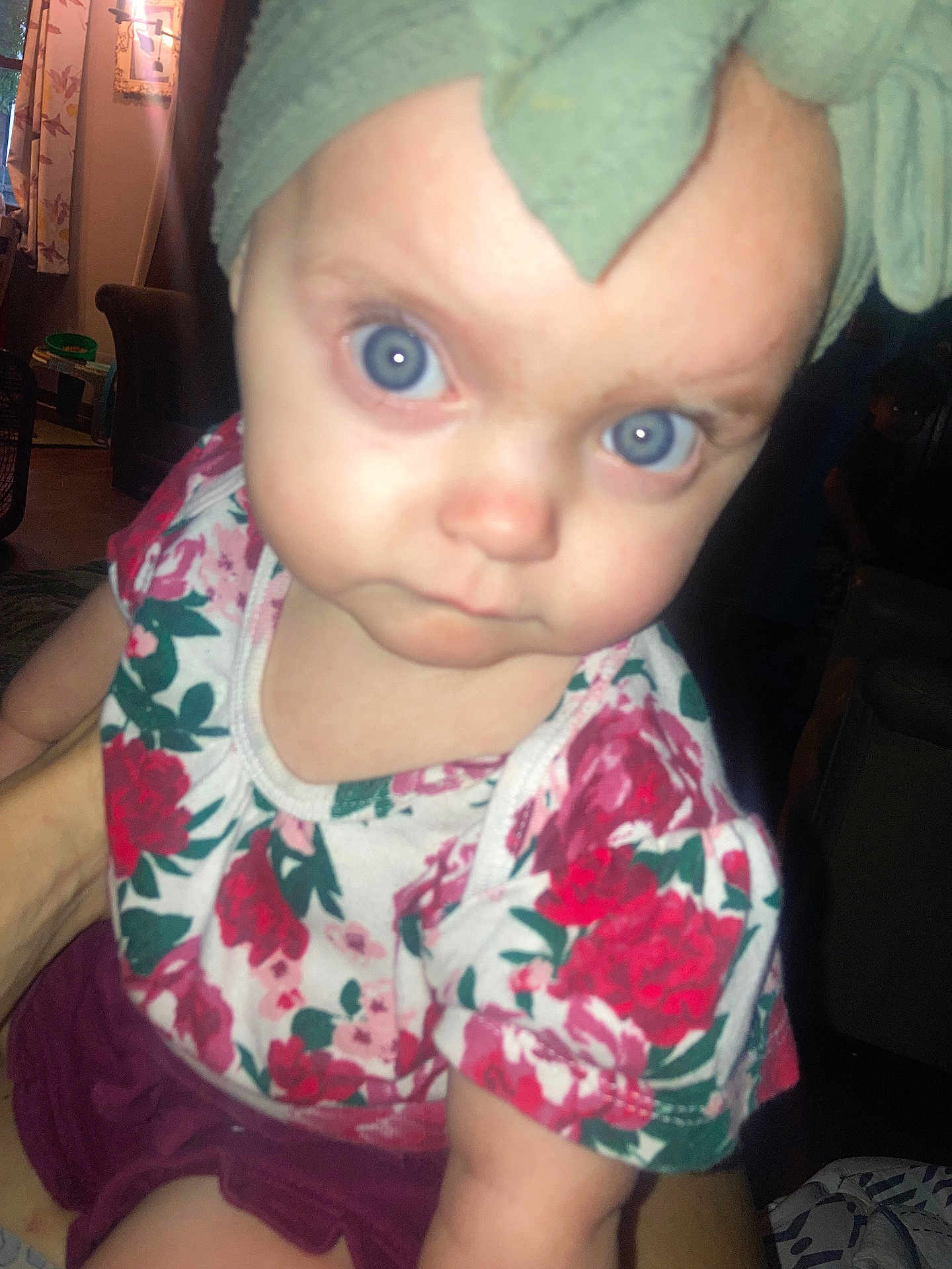 Mazie joined the competition — help win amazing prizes! baby, child, face, blue_eyes, head_wrap, floral_shirt, curious, indoor, dim_lighting, person, portrait, close_up, hand_holding, furniture, home, expression, young, cute, infant, clothing