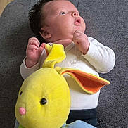 Tiago participe au concours pour gagner de l'argent avec cette photo : baby, infant, plush_toy, yellow, green, blue, white_clothing, couch, gray_fabric, soft_toy, cute, child, indoors, portrait, looking_up, hand_gesture, relaxed, comfort, young_child, home