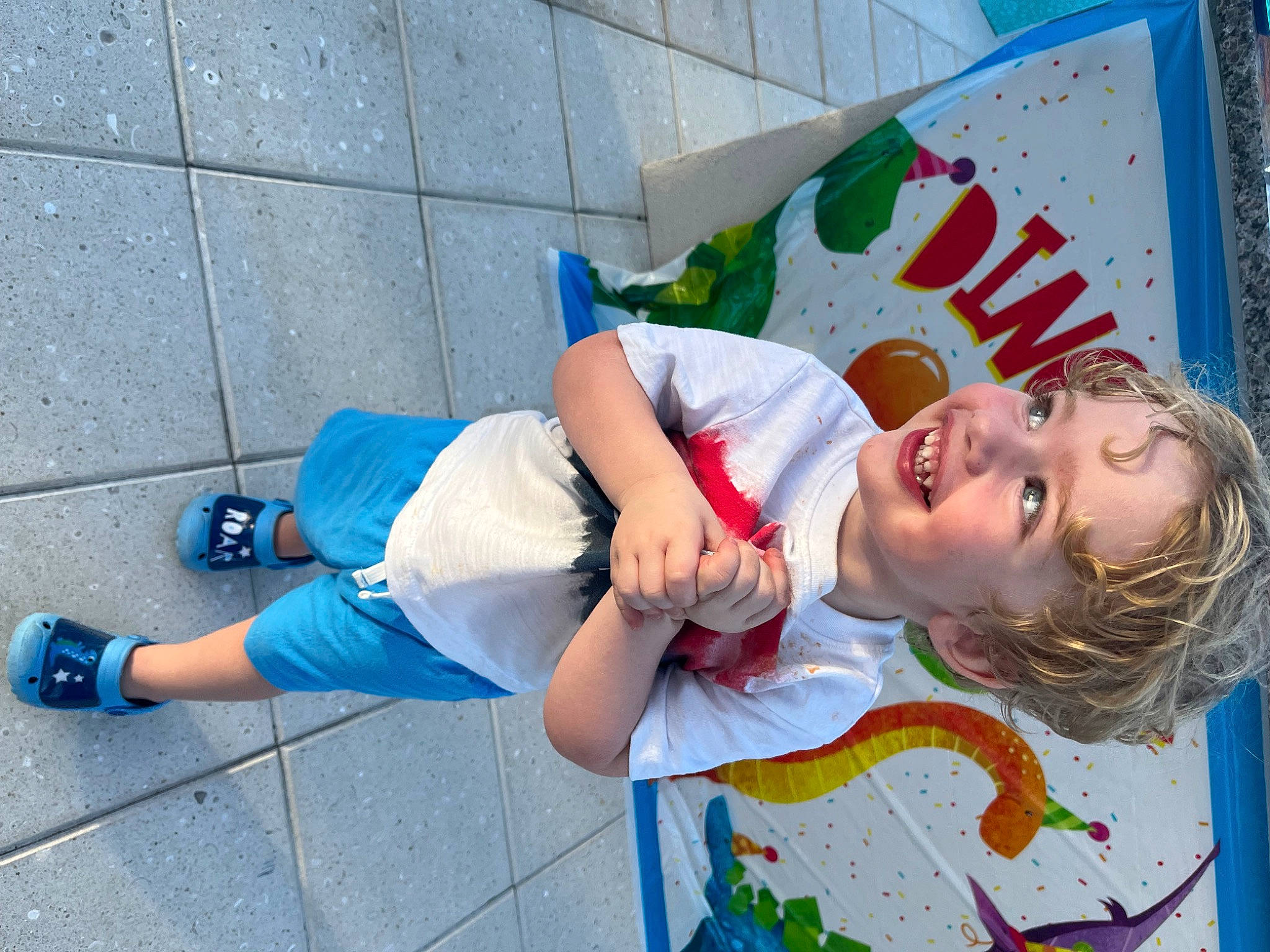 Titan is registered to the contest to win money with this photo: blue, child, electric_blue, event, flooring, fun, happy, human_leg, joy, leisure, person, play, recreation, sandal, shorts, smile, street, t_shirt, textile, thigh