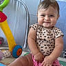 Amelia is registered to the contest to win money with this photo: baby, child, smile, sitting, playpen, toy, colorful, leopard_print, pink_shorts, play_mat, indoor, cute, happy, face, person, infant, hands, legs, looking_at_camera, cheerful