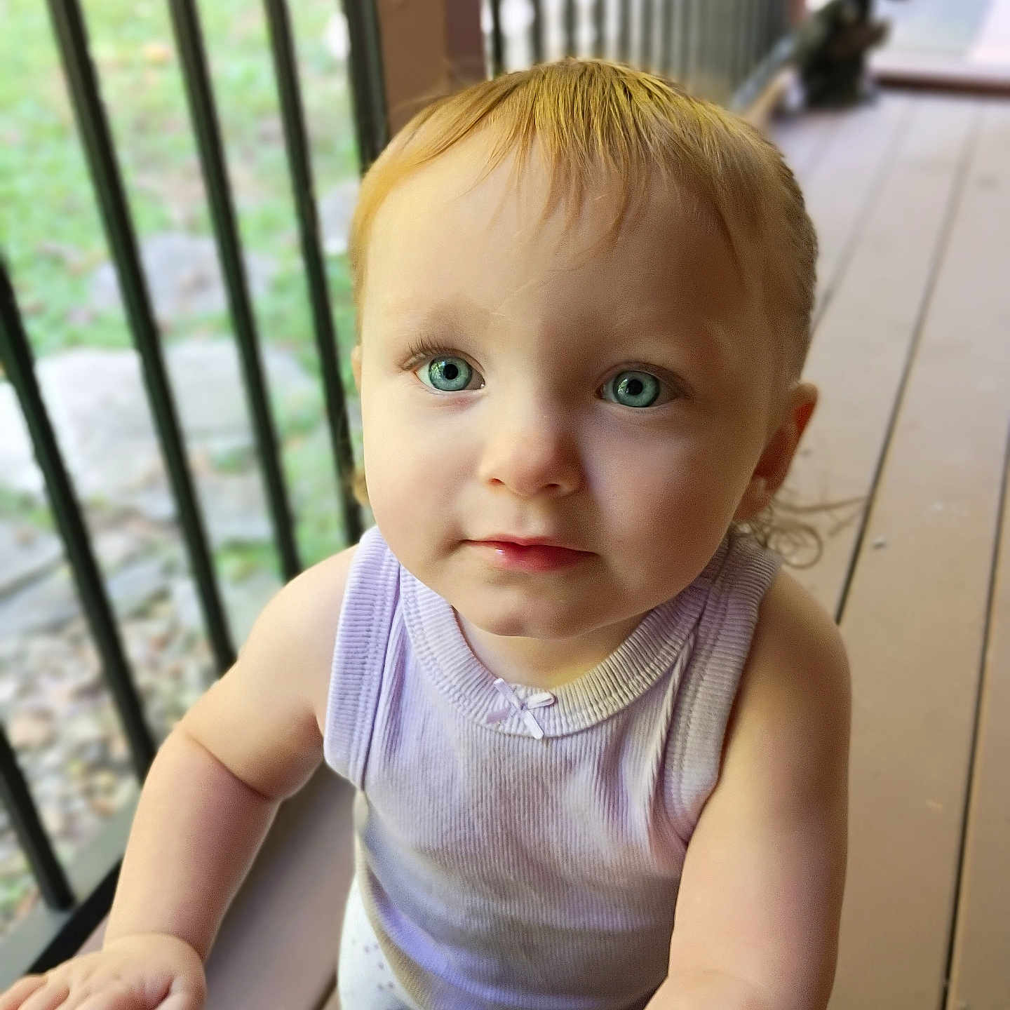 Aria joined the competition — help win amazing prizes! baby, child, toddler, portrait, face, blue_eyes, blond_hair, looking_at_camera, serious_expression, outdoor, deck, balcony, railing, wooden_floor, sunlight, sleeveless_shirt, lavender_clothing, gray_pants, toy, close_up