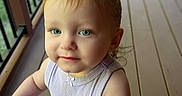 Aria joined the competition — help win amazing prizes! toddler, child, baby, portrait, face, blond_hair, blue_eyes, looking_at_camera, outdoor, deck, wooden_floor, railing, blue_table, sleeveless_shirt, sitting, standing, daylight, home, close_up, candid