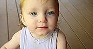Aria is registered to the contest to win money with this photo: baby, blonde_hair, blue_eyes, blue_object, child, close_up, eyes, face, floor, hands, home, indoors, looking_at_camera, natural_light, neutral_expression, portrait, sleeveless_shirt, standing, toddler, wooden_floor