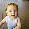 Aria is registered to the contest to win money with this photo: toddler, child, baby, portrait, indoors, wooden_floor, blue_object, sleeveless_shirt, blonde_hair, blue_eyes, face, eyes, hands, standing, looking_at_camera, neutral_expression, home, floor, natural_light, close_up