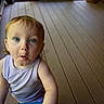 toddler, child, baby, portrait, indoors, wooden_floor, blue_table, sleeveless_shirt, blond_hair, blue_eyes, wide_eyed, surprised_expression, open_mouth, sitting, standing, candid, natural_light, home, background, photography