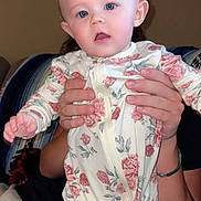 Embri is registered to the contest to win money with this photo: baby, child, infant, person, hands, floral_clothing, onesie, blue_eyes, indoor, couch, blanket, portrait, cute, holding, young_child, human, face, skin, sitting, cozy