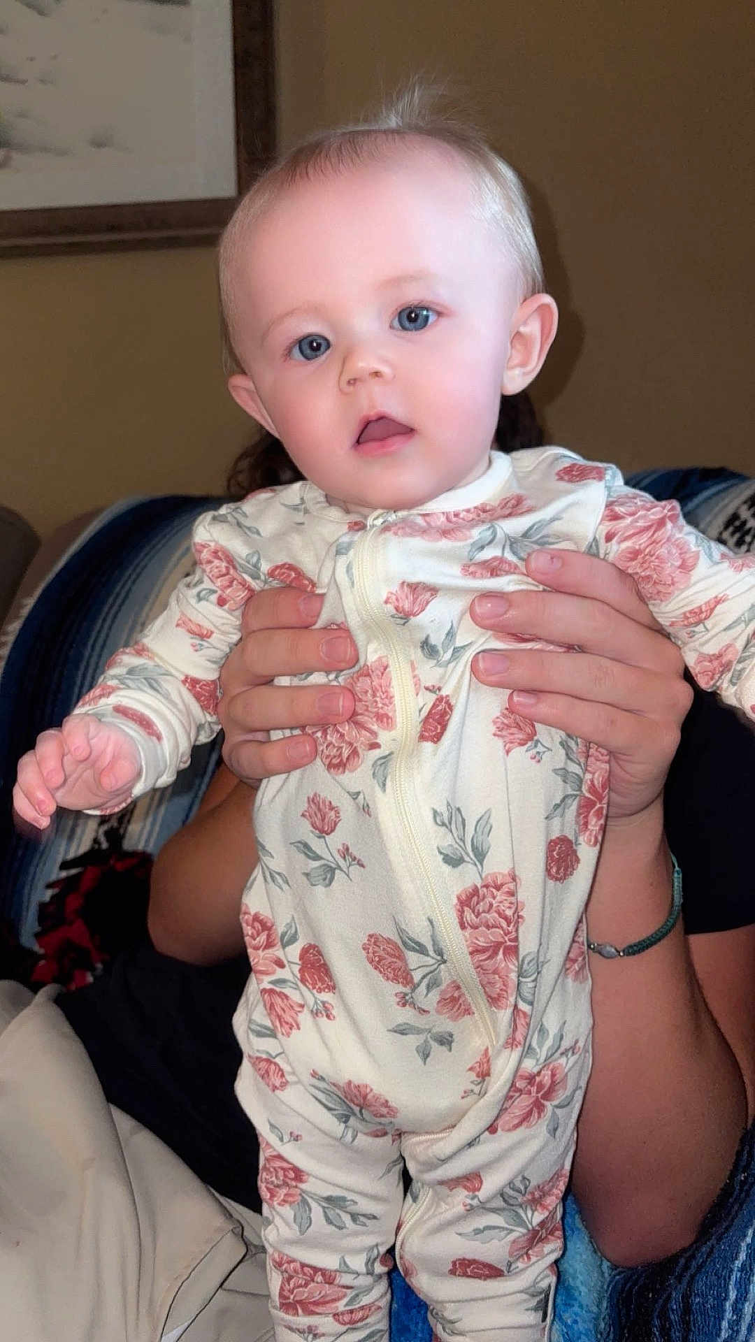 Embri is registered to the contest to win money with this photo: baby, child, infant, person, hands, floral_clothing, onesie, blue_eyes, indoor, couch, blanket, portrait, cute, holding, young_child, human, face, skin, sitting, cozy