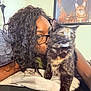 person, cat, tortoiseshell_cat, glasses, curly_hair, indoor, cuddle, portrait, furniture, blanket, framed_picture, animal, pet, face, closeup, home, cozy, affection, blur, living_room