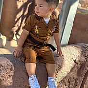 Raymundo is registered to the contest to win money with this photo: child, toddler, boy, portrait, outdoor, sitting, rock, nature, sunlight, brown_outfit, jumpsuit, giraffe_patch, sneakers, white_shoes, belt, short_hair, looking_away, face, playful, adventure