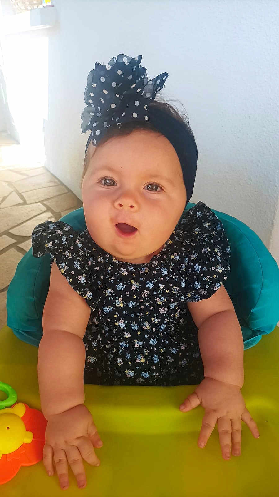 Eliana participe au concours pour gagner de l'argent avec cette photo : baby, child, infant, headband, polka_dot, dress, floral_pattern, sitting, baby_seat, toy, hands, face, expression, surprised, indoor, wall, floor, bright, cute, portrait