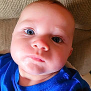 Skyler is registered to the contest to win money with this photo: baby, blue_shirt, face, closeup, child, infant, couch, texture, skin, eyes, portrait, expression, indoors, person, young_child, curious, head, clothing, sitting, cute