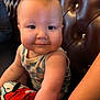 Charlie joined the competition — help win amazing prizes! baby, child, infant, plush_toy, snoopy, leather_bench, tufted_furniture, smiling, cute, indoors, soft_lighting, person, arm, clothing, patterned_outfit, face, cheeks, happy, toy, seated