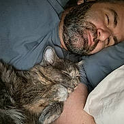 Woofie joined the competition — help win amazing prizes! man, beard, cat, sleeping_cat, lying_down, arm, bed, pillow, cozy, indoor, resting, pet, animal, furry, closeup, comfort, relaxed, snuggling, human, casual_clothing
