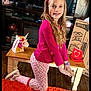 Teagan is registered to the contest to win money with this photo: child, girl, pink, heart_headband, long_hair, smile, orange_rug, pajama_pants, sneakers, living_room, television, unicorn_box, bench, wood_floor, watch, party_decor, cardboard_box, toy, portrait, standing_pose
