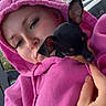 woman, puppy, dog, chihuahua, pet, cuddling, hoodie, pink_clothing, selfie, portrait, face, long_eyelashes, outdoor, trees, building, hand, small_dog, black_and_tan, adorable, companionship