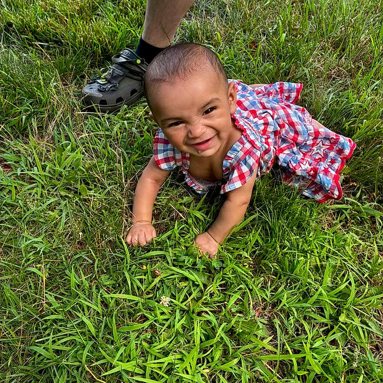 Jezimae is registered to the contest to win money with this photo: baby, casual, child, crawling, cute, expression, footwear, grass, grass_field, greenery, happy, infant, legs, nature, outdoor, person, plaid_dress, playful, smiling, summer