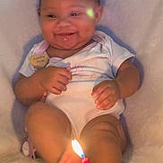 Aurelia is registered to the contest to win money with this photo: baby, child, smiling, birthday_candle, candle_flame, cupcake, dimples, white_clothing, sitting, soft_surface, celebration, closeup, cute, infant, indoors, happy, small_hands, legs, face, warm_light
