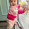 baby, child, colorful_clothing, curious, cute, expression, face, floor, foot, glass_door, headband, home, indoors, natural_light, pink_bow, portrait, standing, warm_colors, window, young_child