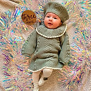 Hazel is registered to the contest to win money with this photo: baby, infant, knitted_clothing, hat, blanket, streamers, milestone_sign, three_months, cute, portrait, lying_down, soft_texture, white_tights, face, child, celebration, closeup, indoors, festive, smiling