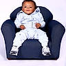 William joined the competition — help win amazing prizes! toddler, child, armchair, blue_clothing, curly_hair, sneakers, smiling, casual, indoor, studio, portrait, baby, young_child, seated, white_background, comfortable, fashion, relaxed, cute, person