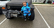 William joined the competition — help win amazing prizes! toddler, child, blue_clothing, jeep, vehicle, parking_lot, apartment_building, outdoor, curious, black_vehicle, bumper, tire, asphalt, urban, person, casual, daytime, small_child, vehicle_front, jeep_grille